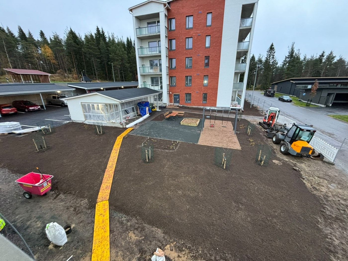 Kerrostalon piha maanrakennusvaiheessa, uudet kulkureitit ja kone työssä