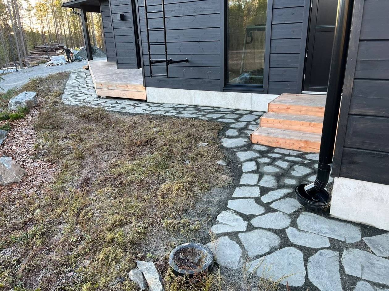Luonnonkivipolku kaartuu tumman talon sivustalle portaiden luota
