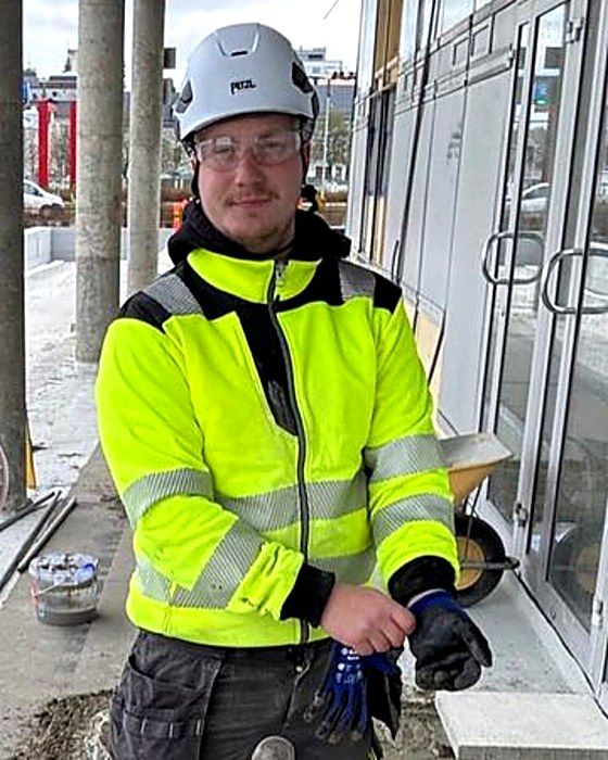 Toinen veljeksistä keltaisessa huomiotakissa työmaalla rakennuksen edessä